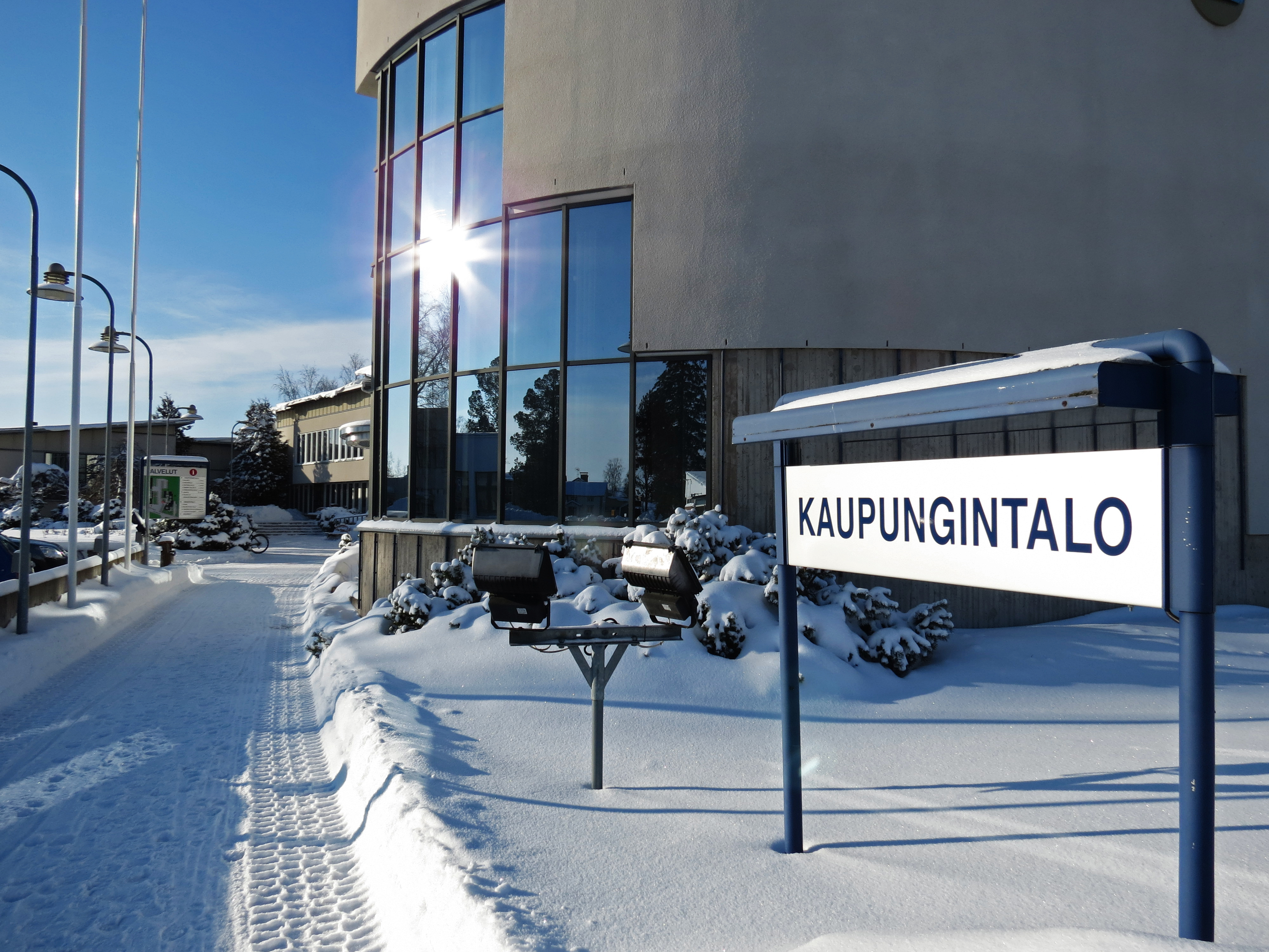 Kuva Kalajoen kaupungintalon sisääntulosta ja opasteesta lumisessa auringonpaisteessa.