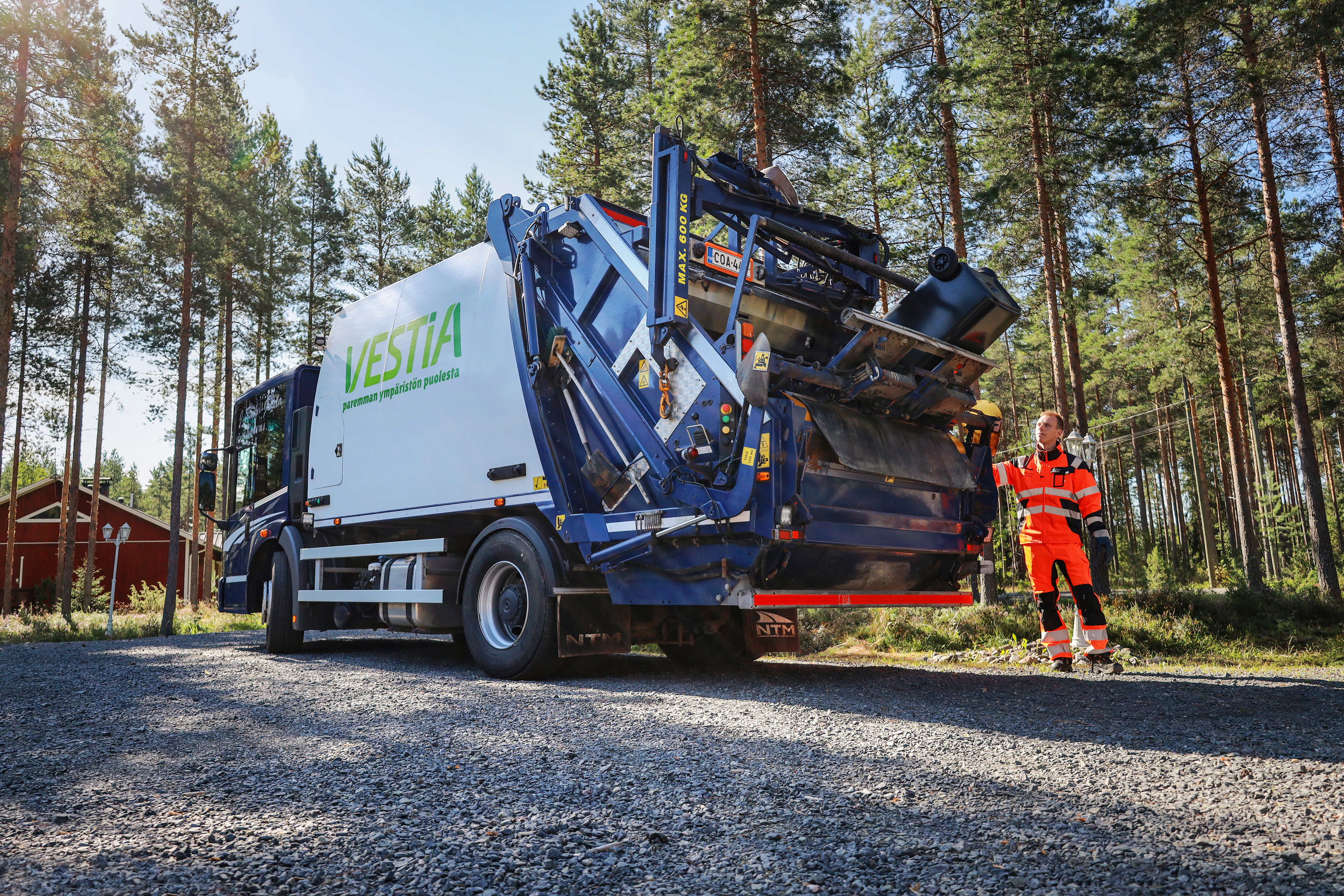 Kuvassa Vestia Oy:n jäteauto soratiellä seisahtuneena kuljettaja vieressään.