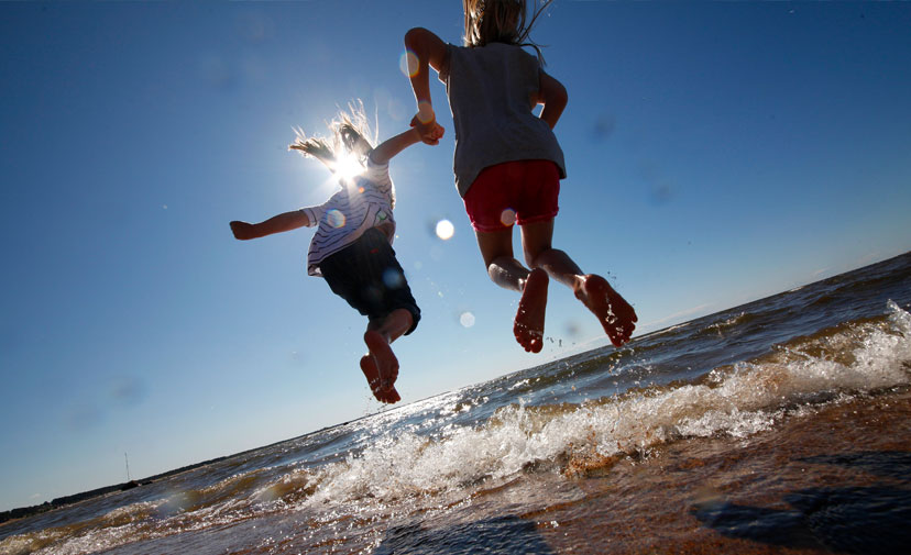Kaksi lasta hyppii vedessä auringon paistaessa.