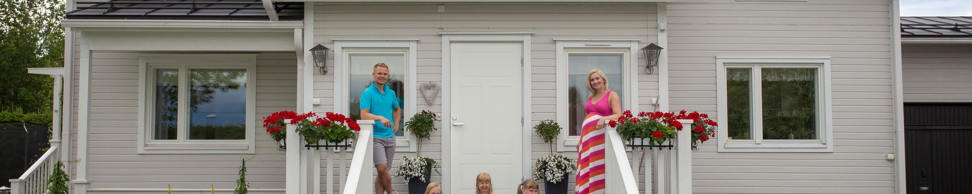 Kuvassa omakotitalo, perhe ulkoportailla. Isä, äiti ja kolme lasta.