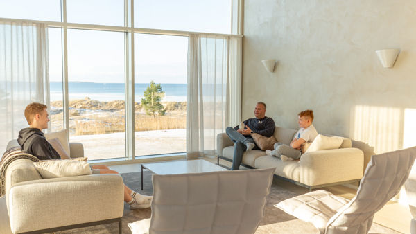 Kuvassa olohuoneessa kolme ihmistä sohvalla istumassa, merinäköala ikkunasta.