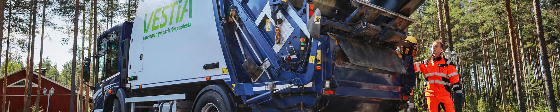 Kuvassa Vestia Oy:n jäteauto soratiellä seisahtuneena kuljettaja vieressään.