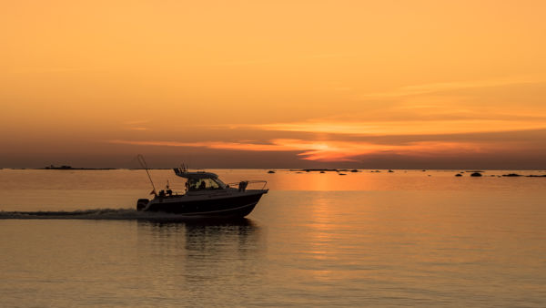 Auringonlaskun värjäämä oranssi merimaisema ja vene.