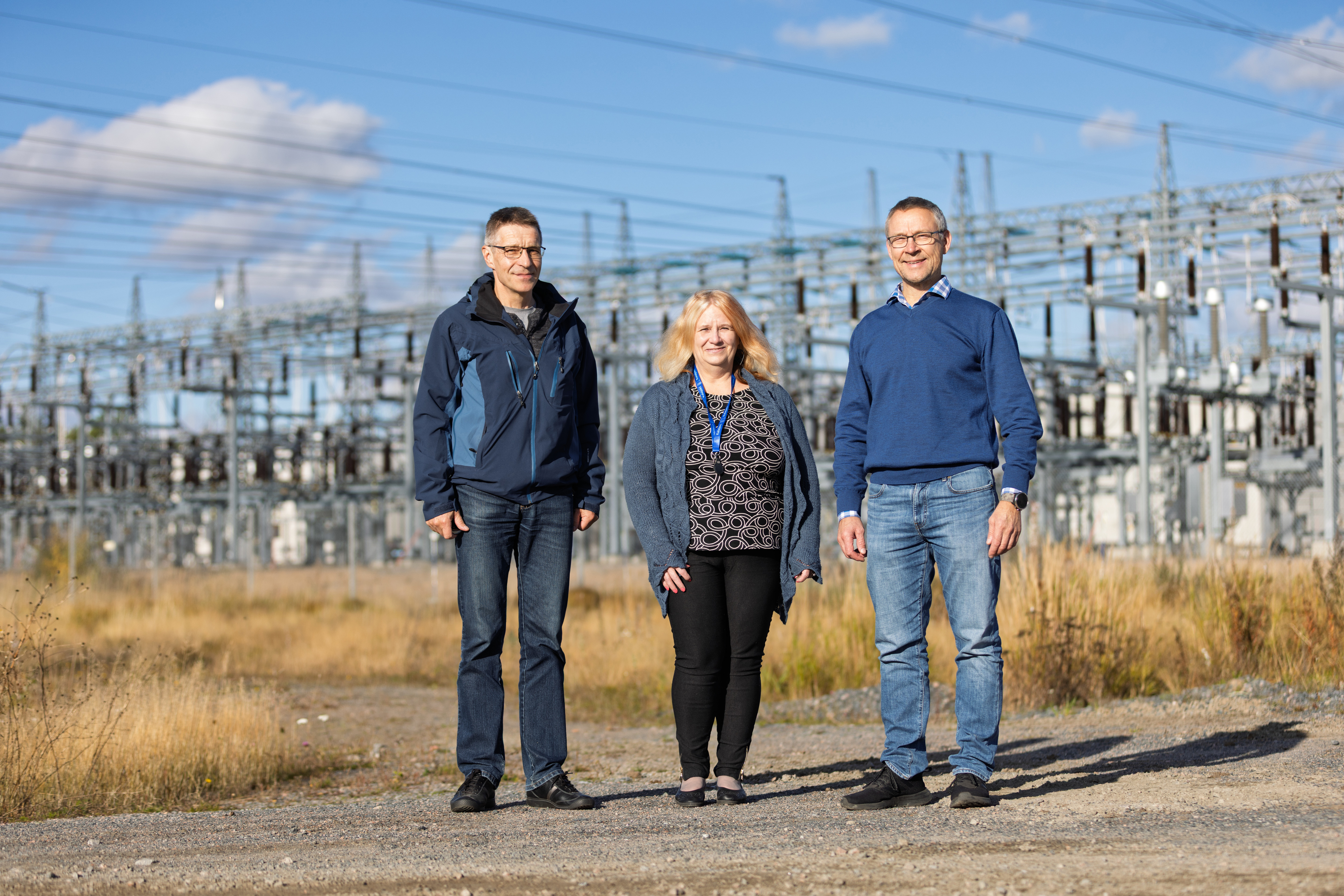 Kolme ihmistä seisoo muuntajan edessä.