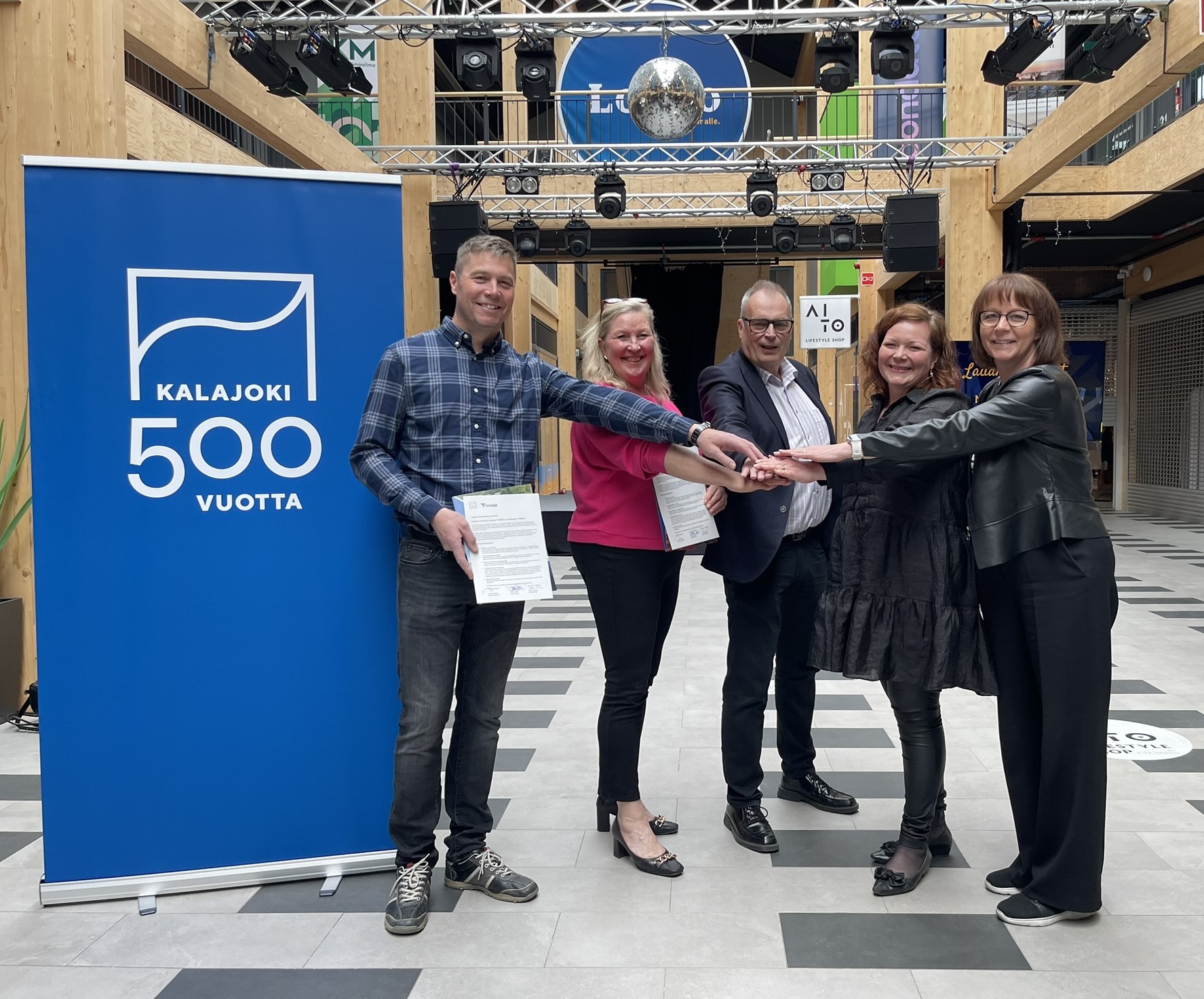viisi henkilöä hymyilee kuvassa ja kättelevät