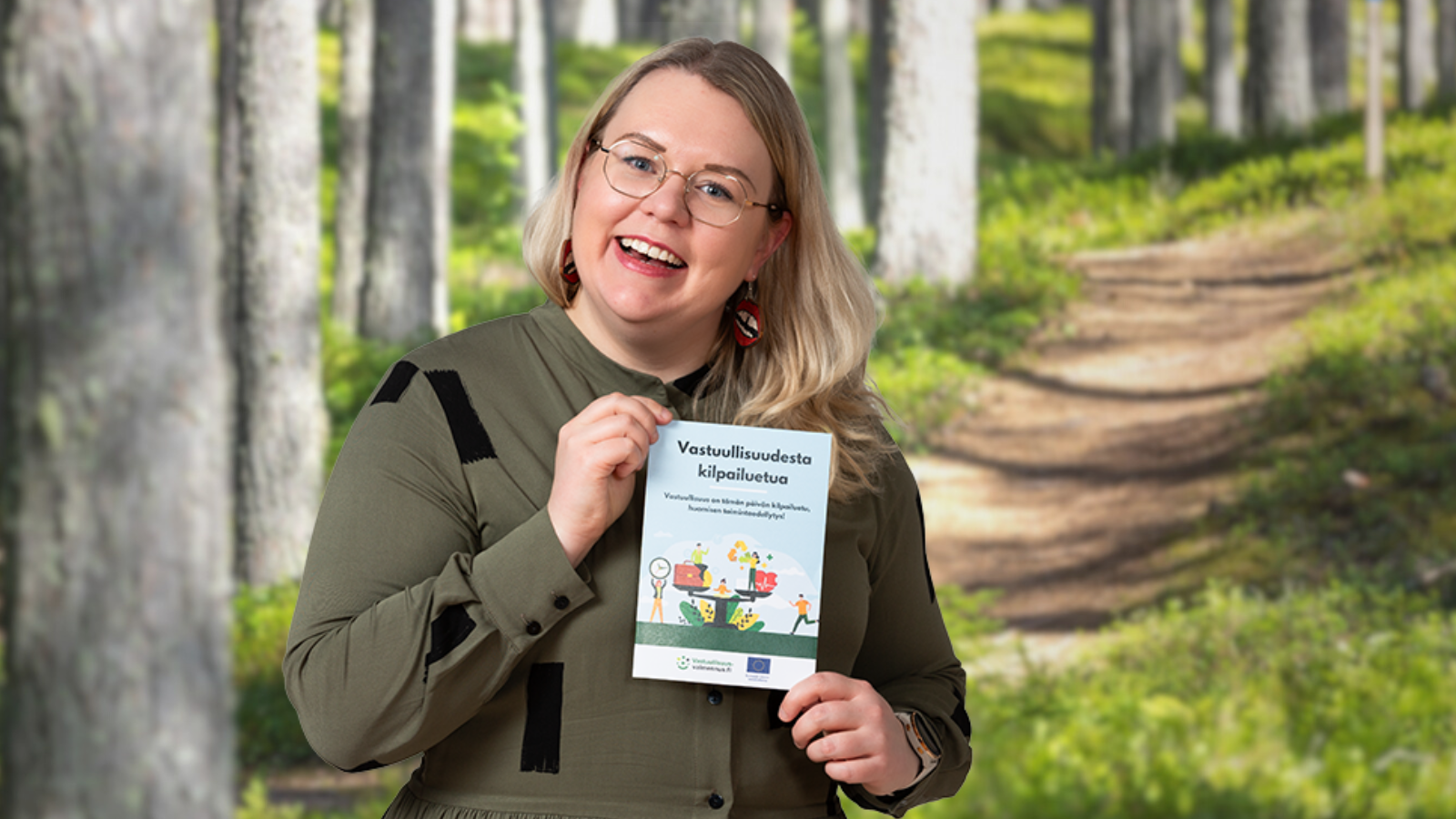 Anna Uusitalo pitelee esitettä metsämaisemassa.