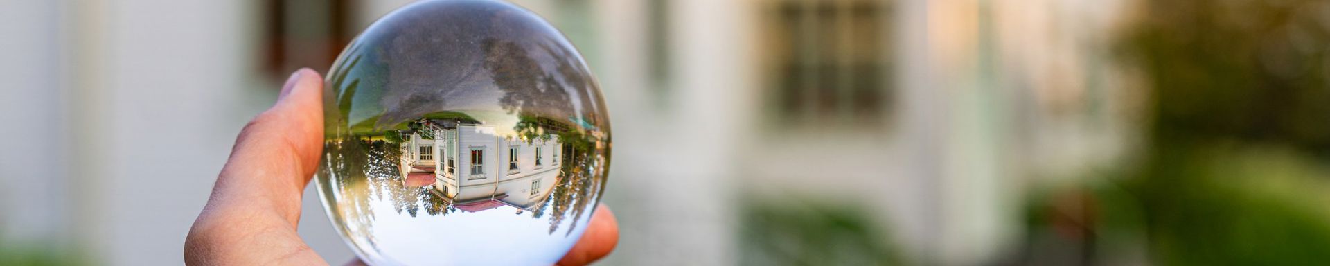 Käsi pitää lasikuulaa, johon heijastuu Havulan vanha rakennus.