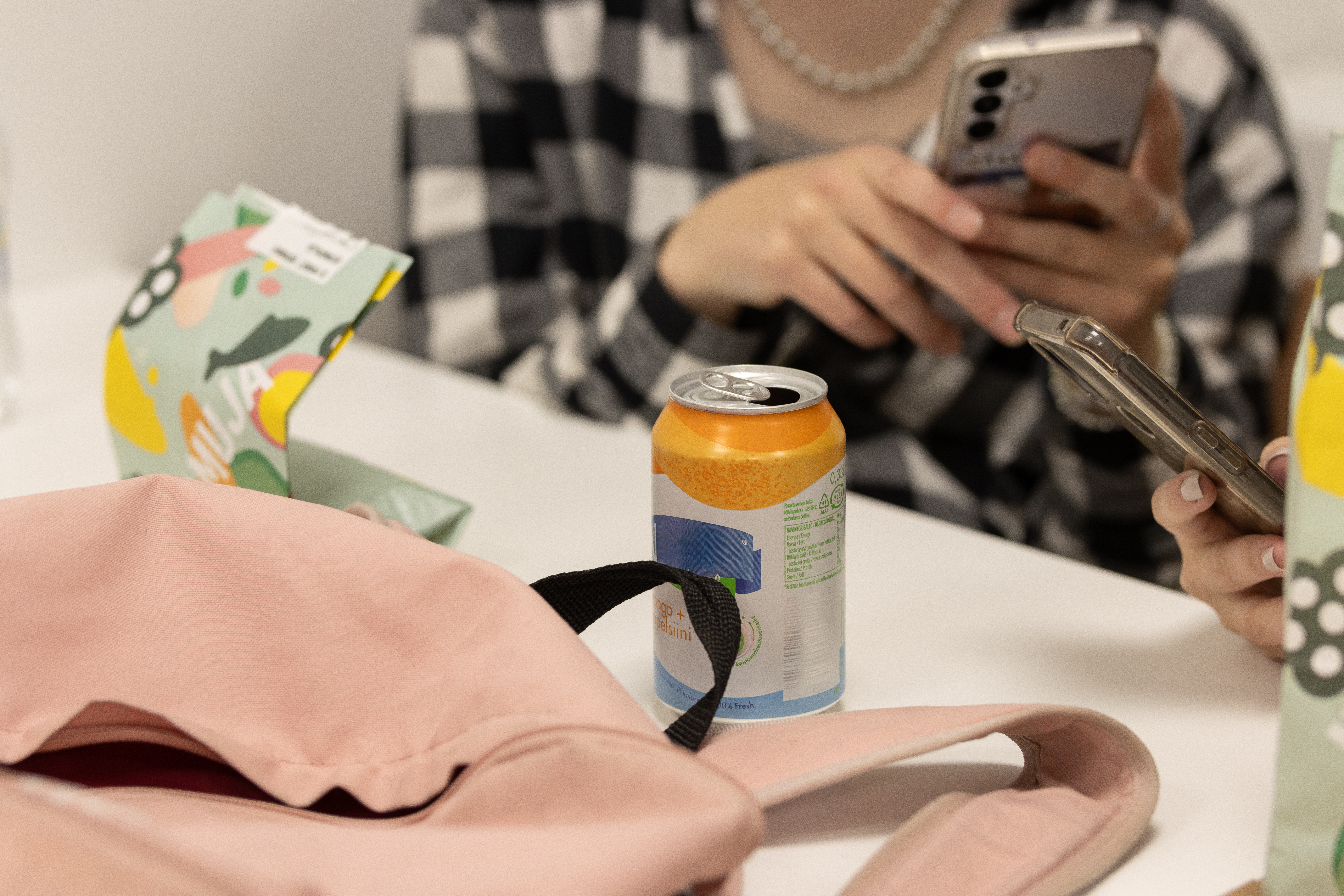 Nuori selaa puhelinta ja pöydällä on herkkuja.