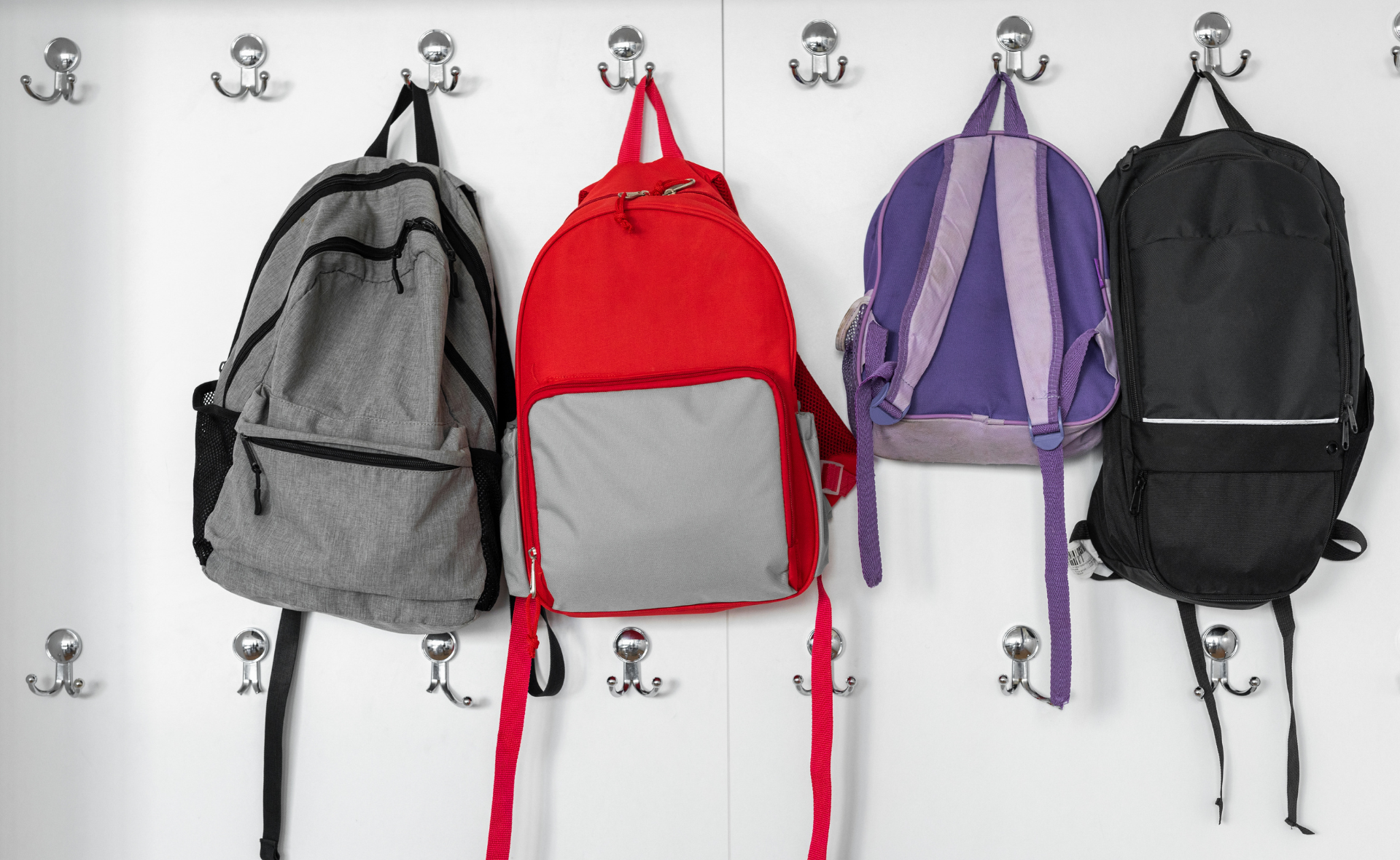 Eri värisiä reppuja naulakossa.