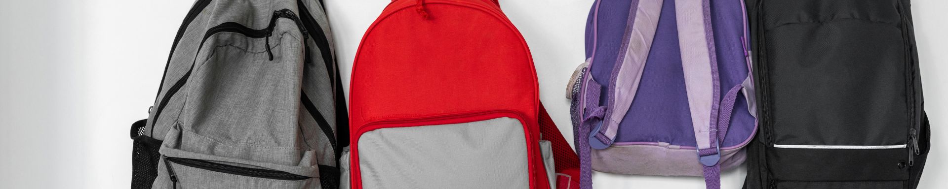 Eri värisiä reppuja naulakossa.