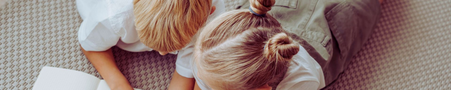 Kaksi lasta makaa lattialla ja toinen kirjoittaa vihkoon.