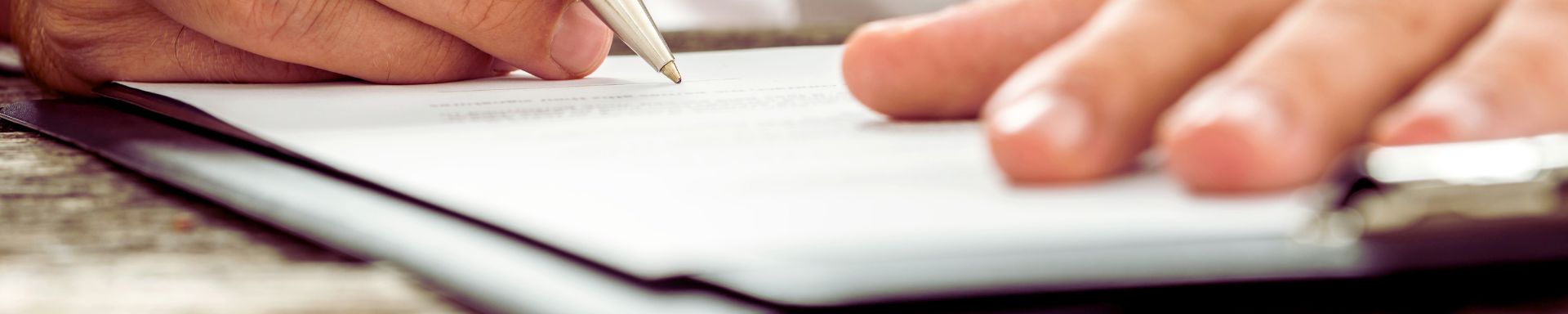 Paperipino pöydällä, jota kädet pitelevät ja kirjoittavat kynällä tekstiä.