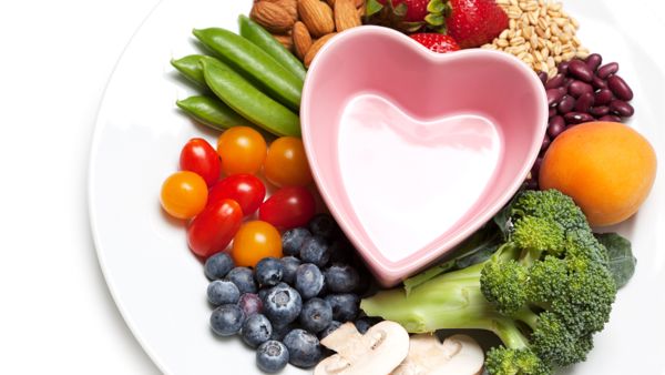 Kasviksia, marjoja ja siemeniä sydämenmuotoisen lautasen ympärillä.