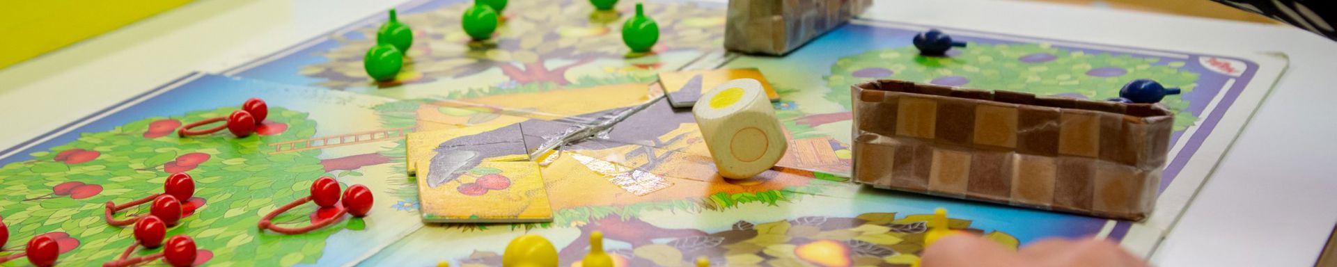 Pelilauta ja värikkäät pelinappulat, joita kädet siirtelee.