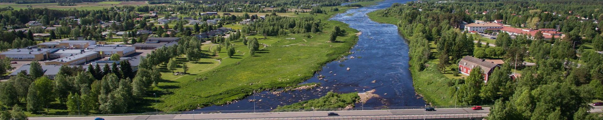 Vihreä jokirantamaisema. Silta keskellä kuvaa ja taustalla meri.