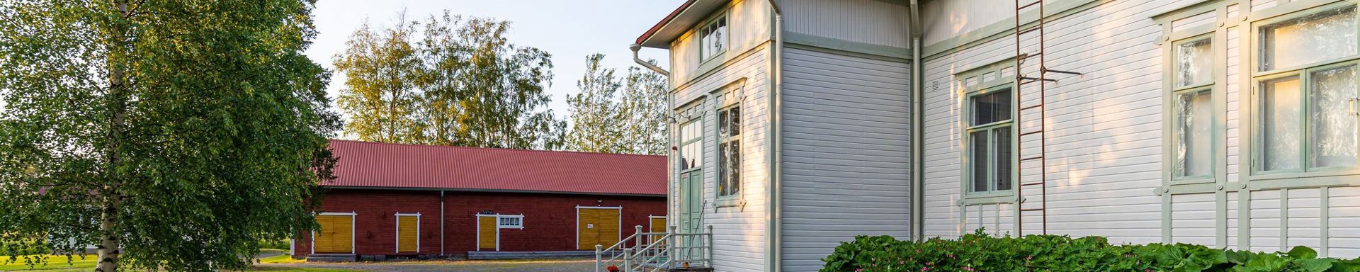 Vanha vaalea iso rakennus ja taustalla punainen ulkorakennus.